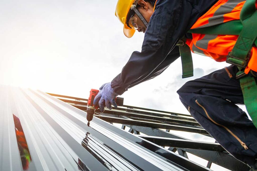 Worker secures a temporary roof tarp while a homeowner observes from a safe distance.