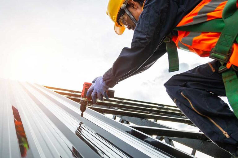Worker secures a temporary roof tarp while a homeowner observes from a safe distance.
